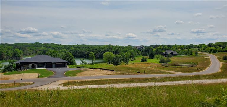 A rural landscape with a farmhouse, fields, and a lake under a clear sky.