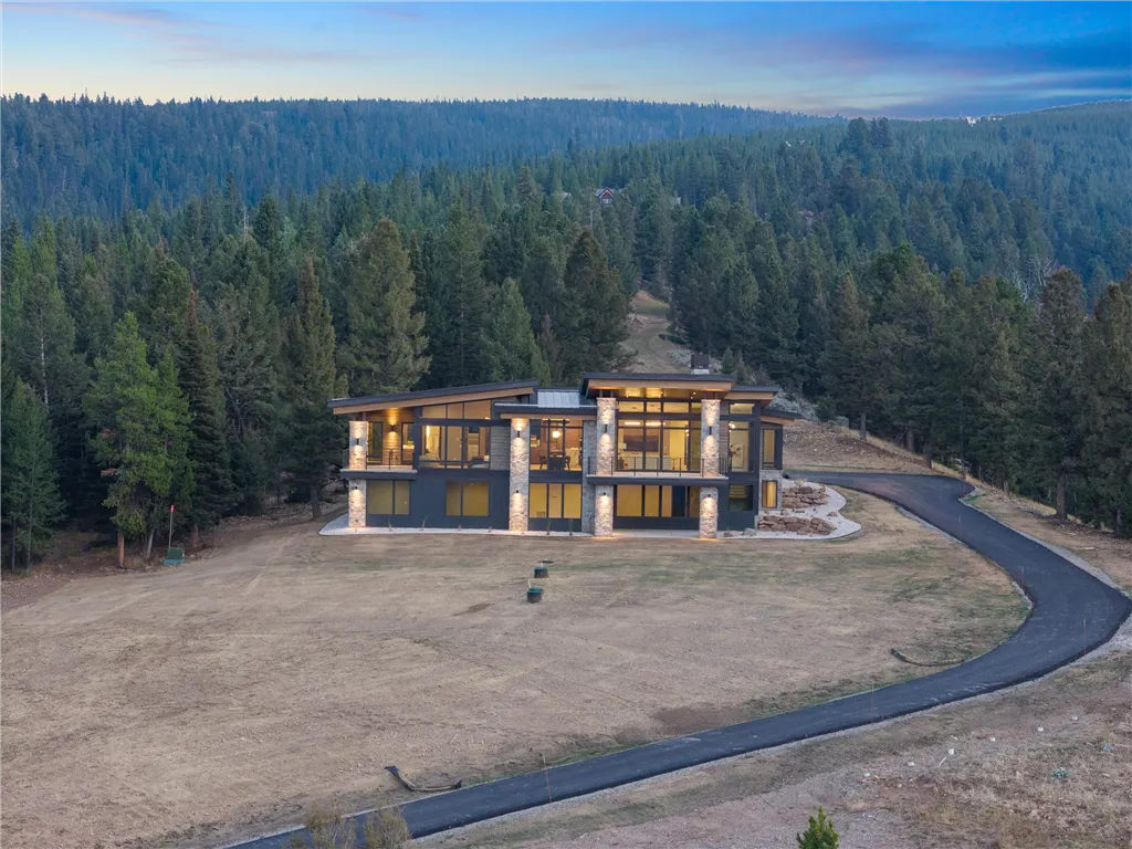Scenic view of a mountain valley with a cabin, lake, and trees.